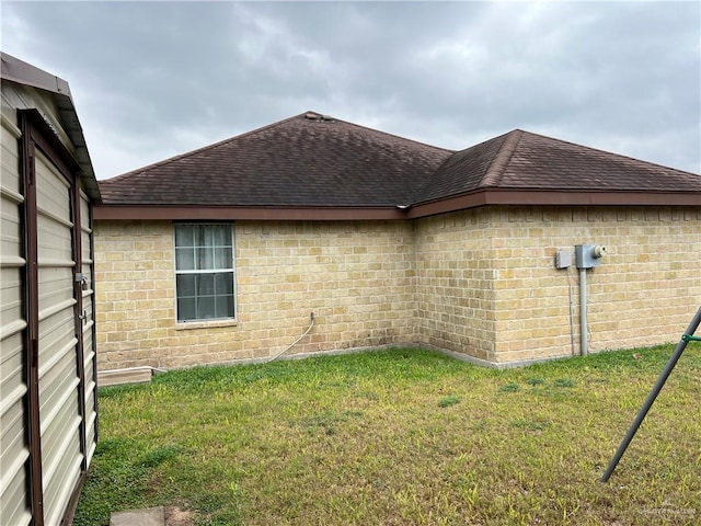 view of property exterior with a yard, brick siding, and roof with shingles