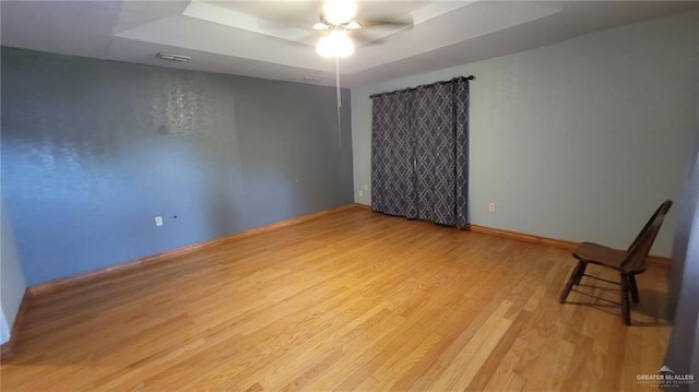 spare room featuring light hardwood / wood-style floors, ceiling fan, and a tray ceiling