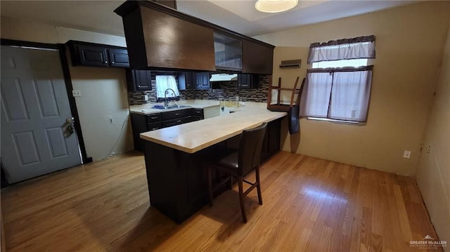 kitchen featuring kitchen peninsula, a kitchen breakfast bar, decorative backsplash, sink, and light hardwood / wood-style floors