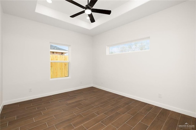 empty room featuring dark hardwood / wood-style floors, ceiling fan, and a tray ceiling