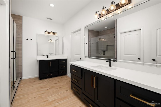 full bath featuring two vanities, a shower stall, visible vents, wood finished floors, and a sink