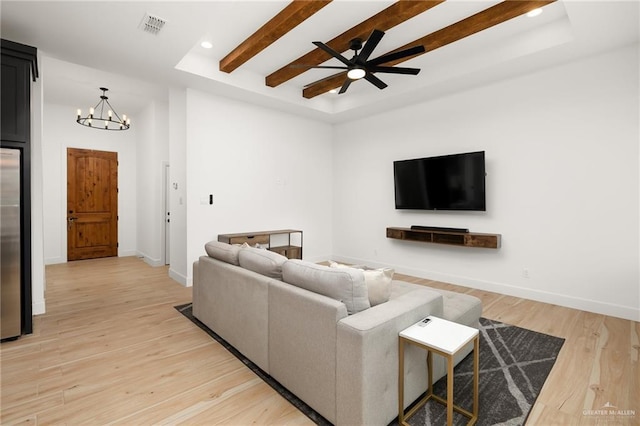 living room featuring visible vents, baseboards, a raised ceiling, light wood-type flooring, and ceiling fan with notable chandelier
