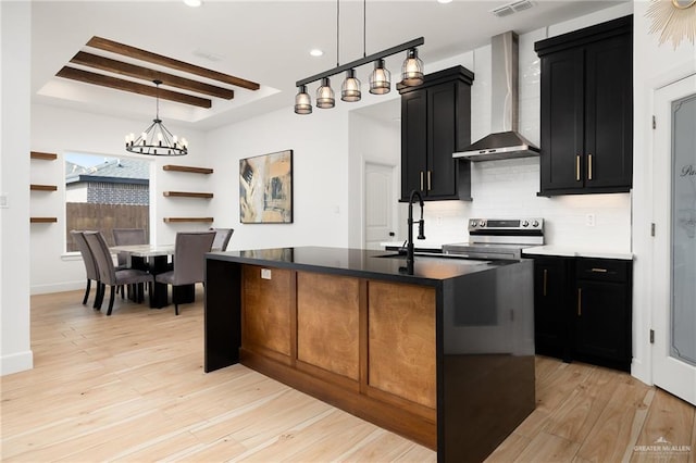 kitchen featuring wall chimney exhaust hood, a sink, light wood-type flooring, dark cabinetry, and stainless steel range with electric cooktop