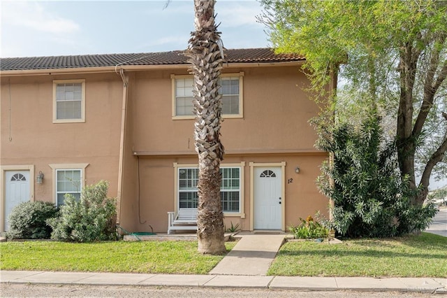 townhome / multi-family property featuring a front yard, a tile roof, and stucco siding