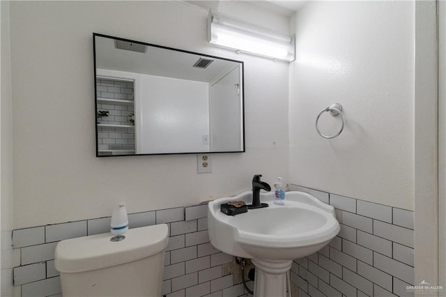 bathroom with toilet, a sink, visible vents, and tile walls