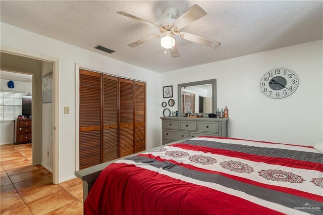 bedroom with light tile patterned floors, a closet, visible vents, a ceiling fan, and a textured ceiling