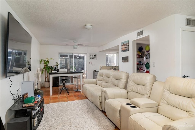 living room with a textured ceiling, ceiling fan, light tile patterned floors, and visible vents