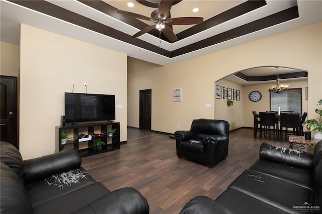 living room with a raised ceiling, ceiling fan with notable chandelier, and dark hardwood / wood-style floors