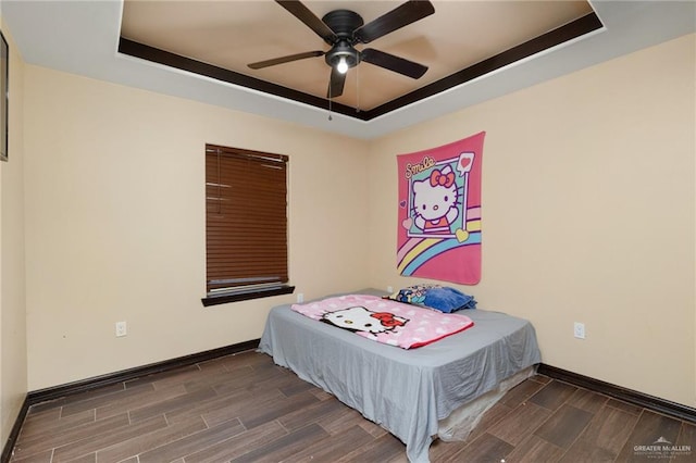 bedroom with ceiling fan, dark wood-type flooring, and a tray ceiling