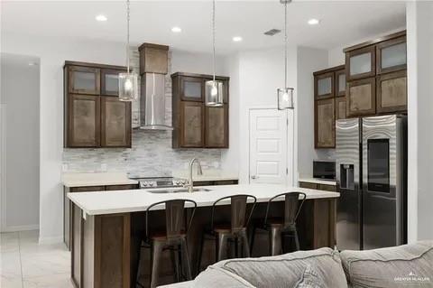 kitchen featuring tasteful backsplash, wall chimney exhaust hood, open floor plan, light countertops, and stainless steel refrigerator with ice dispenser