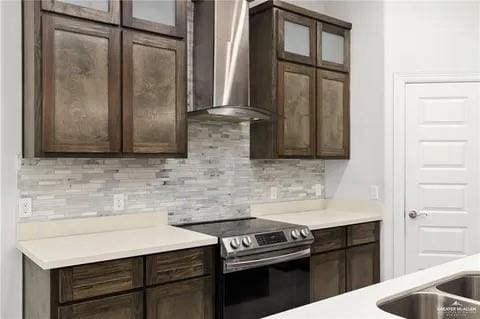 kitchen with tasteful backsplash, dark brown cabinets, wall chimney range hood, and stainless steel electric stove