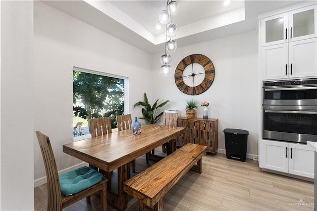 dining area with light wood-type flooring and a tray ceiling