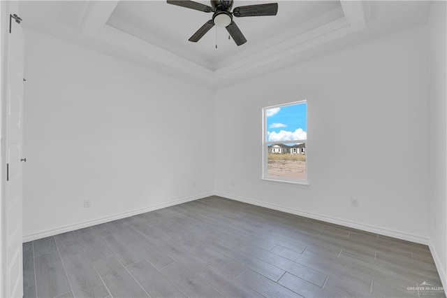 empty room featuring light wood-type flooring, a tray ceiling, and ceiling fan