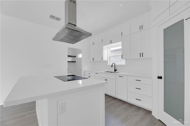 kitchen featuring light wood-type flooring, black electric cooktop, island range hood, sink, and white cabinetry