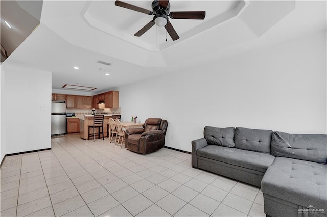 living room featuring baseboards, a tray ceiling, light tile patterned floors, recessed lighting, and a ceiling fan