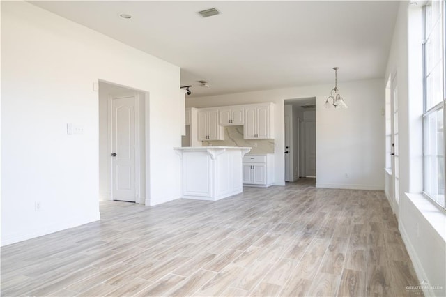 unfurnished living room featuring baseboards, light wood-style flooring, visible vents, and a notable chandelier