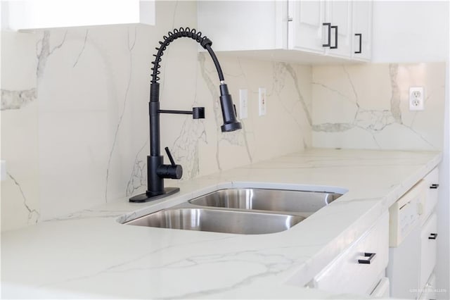 kitchen featuring light stone counters, backsplash, a sink, and white cabinets