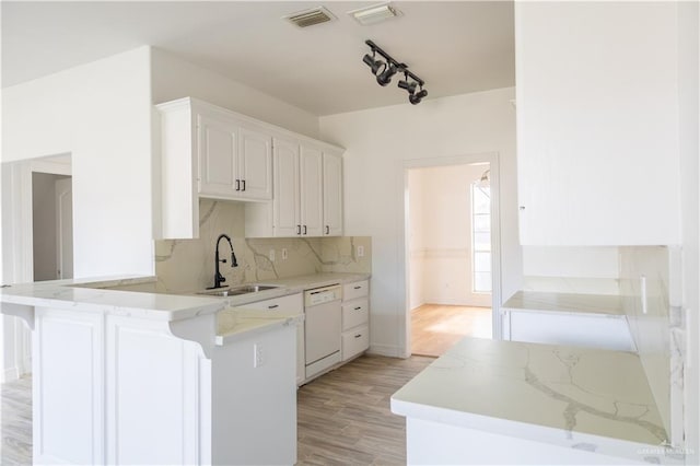 kitchen with a peninsula, a sink, visible vents, dishwasher, and tasteful backsplash