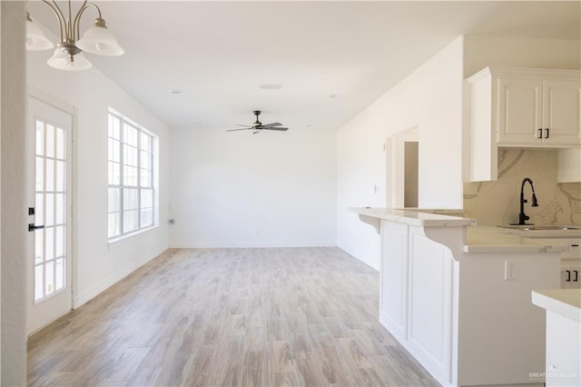 interior space with a sink, white cabinets, light wood-style floors, light countertops, and tasteful backsplash