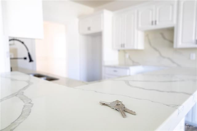 interior details featuring light stone counters, a sink, and white cabinetry