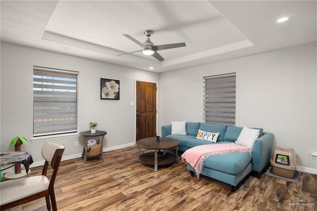 living room featuring hardwood / wood-style flooring, ceiling fan, and a raised ceiling