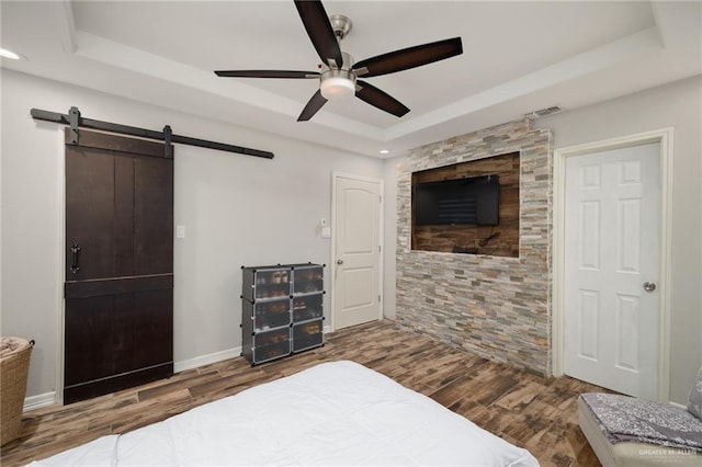 bedroom with a tray ceiling, a barn door, ceiling fan, and hardwood / wood-style flooring