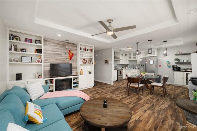 living room with sink, ceiling fan, a raised ceiling, and dark wood-type flooring