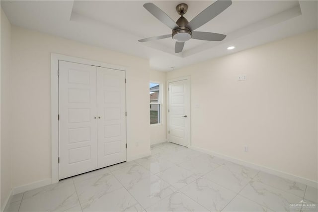 unfurnished bedroom with recessed lighting, a closet, a tray ceiling, marble finish floor, and baseboards