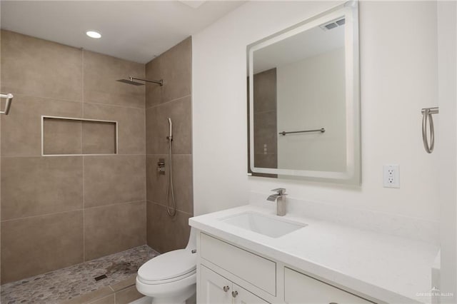 bathroom with toilet, a tile shower, visible vents, and vanity