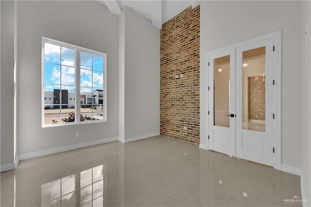 spare room featuring french doors, a towering ceiling, and brick wall