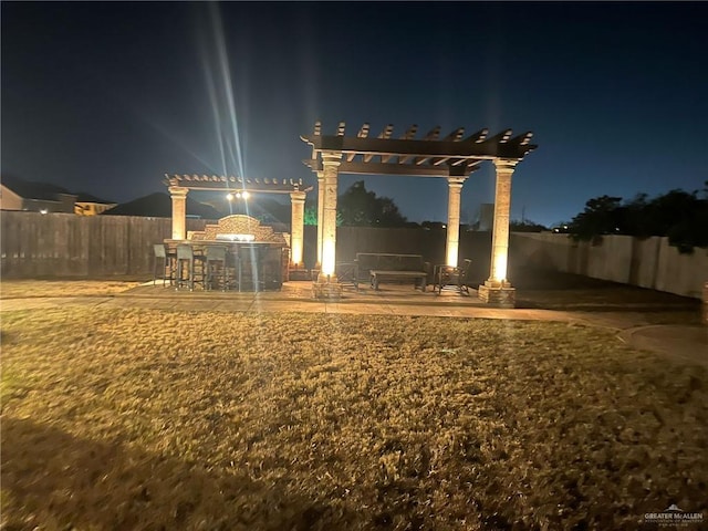 yard at night with a patio area, a fenced backyard, and a pergola