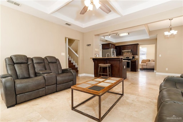 living area with baseboards, visible vents, a raised ceiling, and ceiling fan with notable chandelier