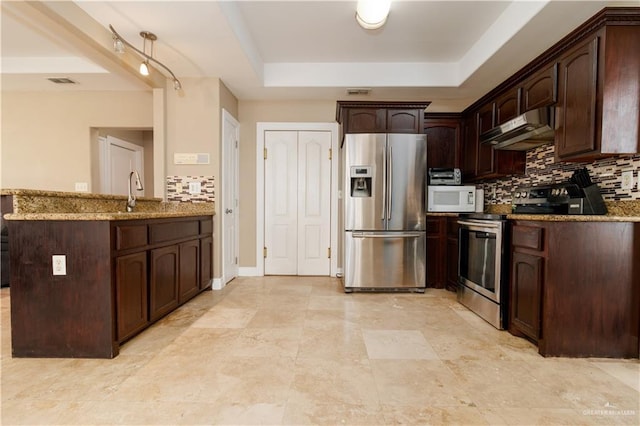 kitchen featuring under cabinet range hood, dark brown cabinets, appliances with stainless steel finishes, a tray ceiling, and tasteful backsplash