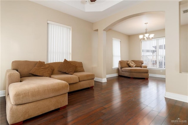 living area featuring arched walkways, dark wood finished floors, baseboards, and ceiling fan with notable chandelier