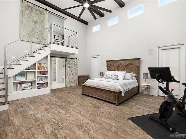 bedroom with beam ceiling, a high ceiling, a barn door, wood finished floors, and baseboards