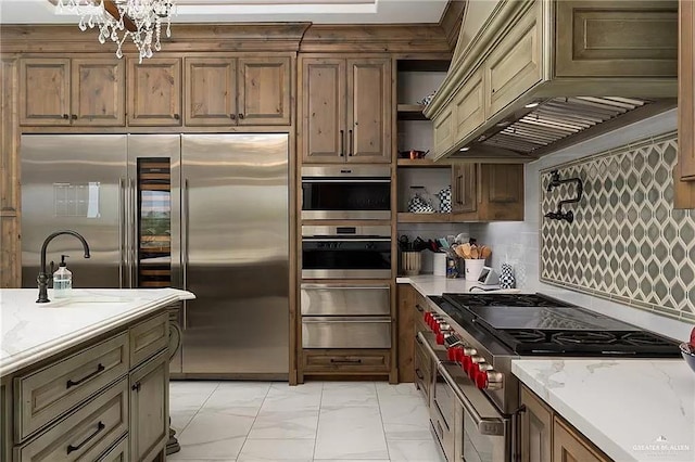 kitchen featuring light stone counters, premium range hood, high quality appliances, marble finish floor, and a warming drawer