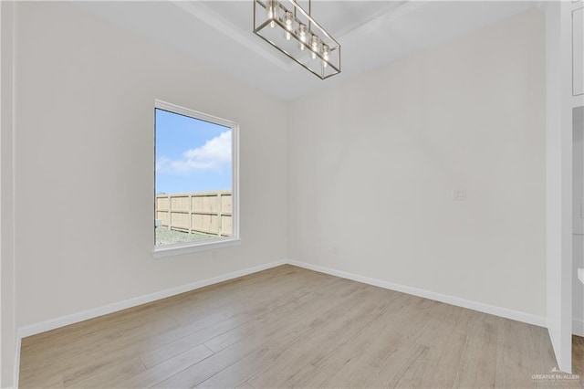 empty room with a chandelier, light wood-type flooring, and baseboards