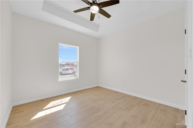 unfurnished room featuring a tray ceiling, baseboards, ceiling fan, and light wood finished floors