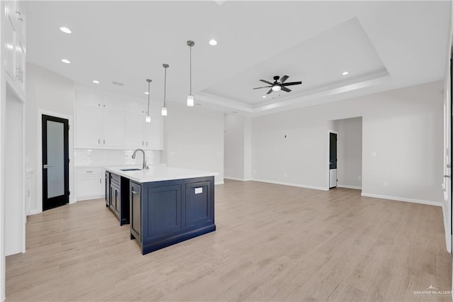 kitchen with a sink, white cabinets, open floor plan, light countertops, and hanging light fixtures