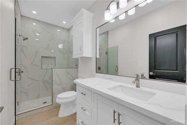 bathroom with a marble finish shower, wood finished floors, vanity, and toilet