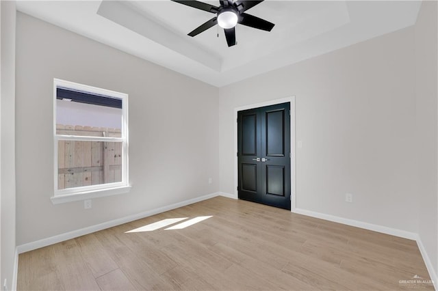 unfurnished bedroom with light wood-type flooring, ceiling fan, baseboards, and a raised ceiling