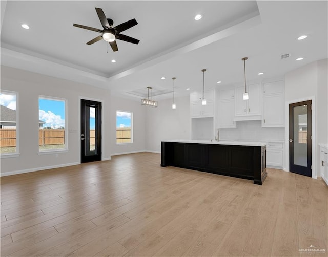 kitchen featuring white cabinets, a large island, open floor plan, a tray ceiling, and light countertops