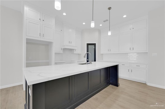 kitchen with light wood-type flooring, pendant lighting, white cabinets, and a sink