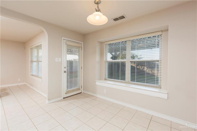 unfurnished dining area featuring arched walkways, baseboards, visible vents, and light tile patterned floors