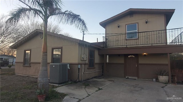 view of front of property featuring a balcony, driveway, central AC, and stucco siding