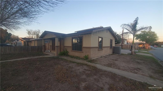 view of side of home with central AC unit, fence, and stucco siding