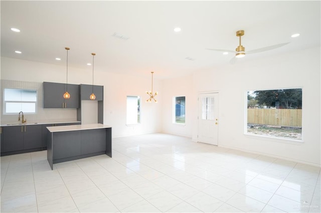 kitchen with plenty of natural light, light tile patterned flooring, ceiling fan with notable chandelier, and sink