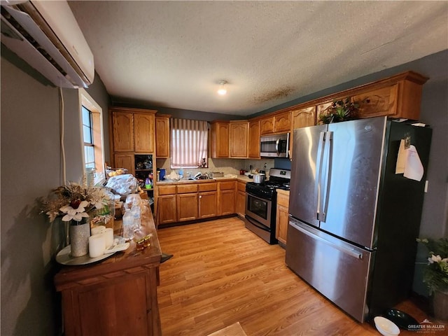 kitchen featuring a wall unit AC, a textured ceiling, light hardwood / wood-style flooring, and appliances with stainless steel finishes