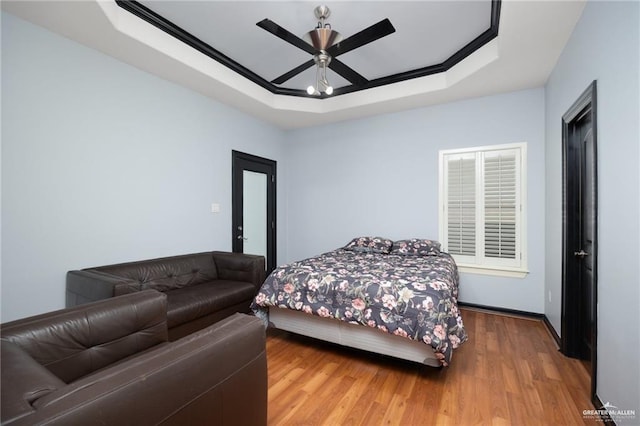 bedroom featuring wood finished floors, a raised ceiling, and a ceiling fan