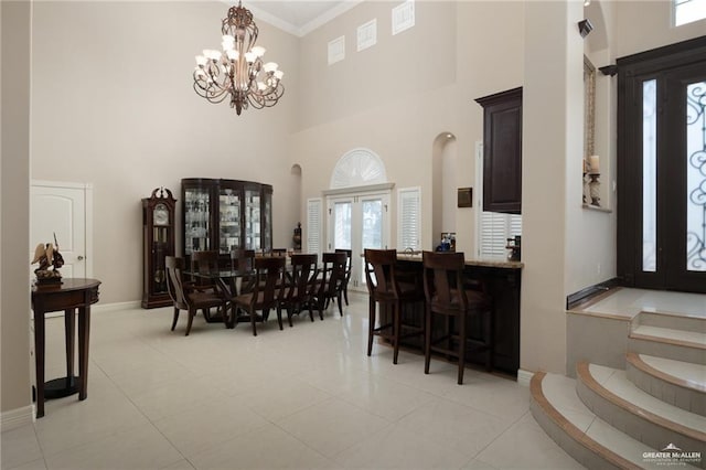 dining space with a chandelier, a high ceiling, baseboards, french doors, and crown molding